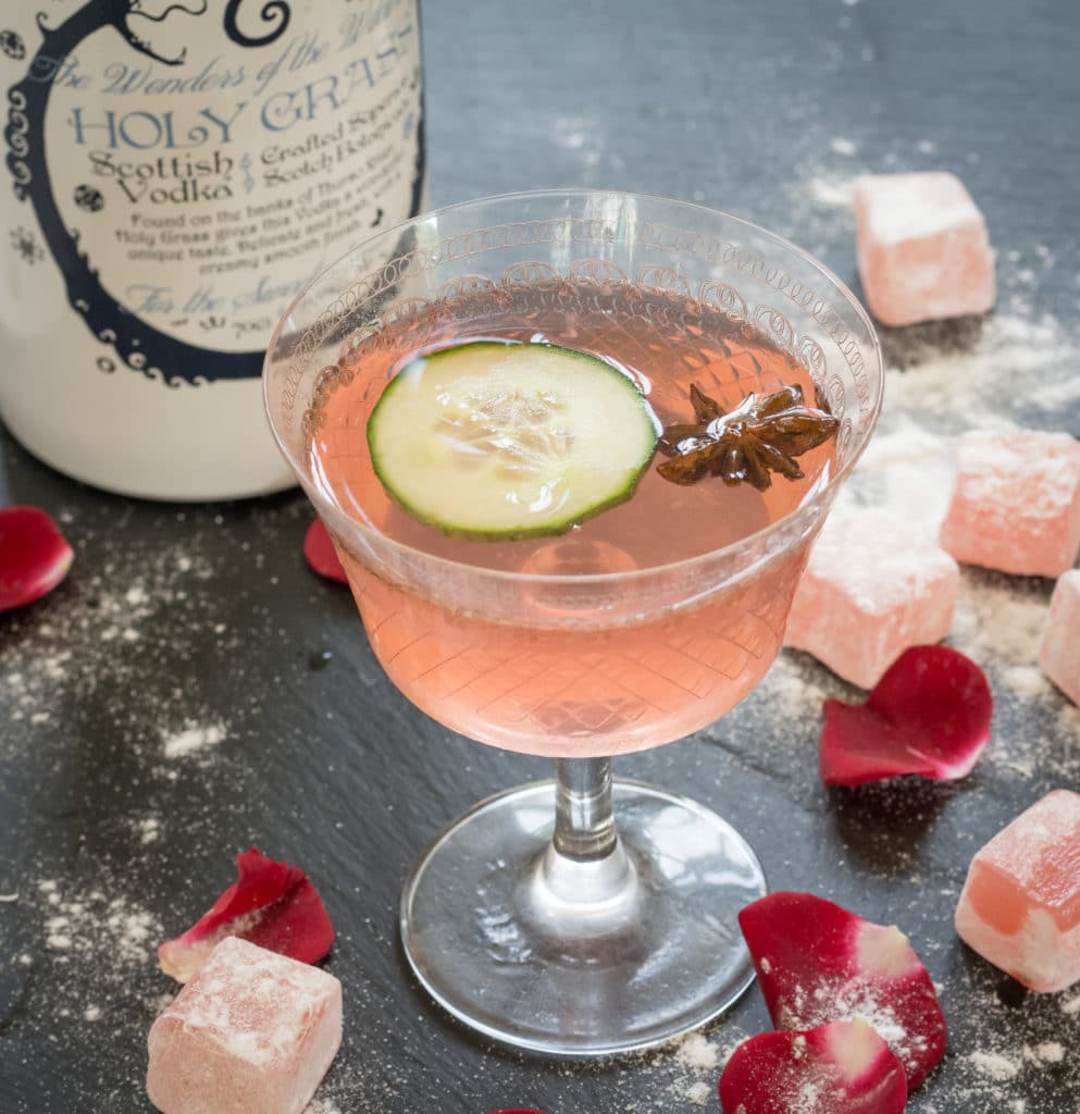 Bottle of Holy Grass Vodka and The Rose Tree cocktail served in a cocktail glass and garnished with a slice of cucumber and star anise seed