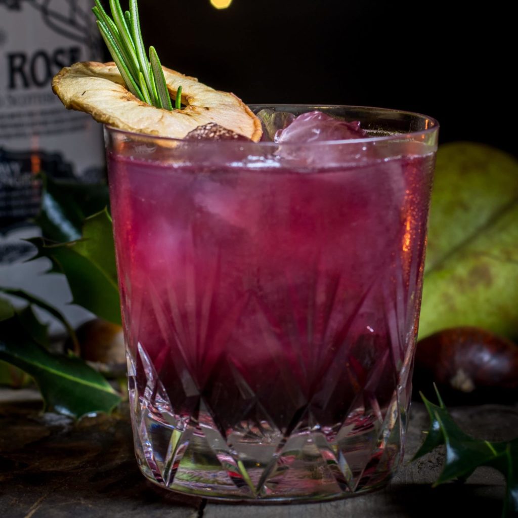 A Partridge in a Pear Tree Xmas Cocktail served in a old fashion glass and garnished with a pear crisp and rosemary