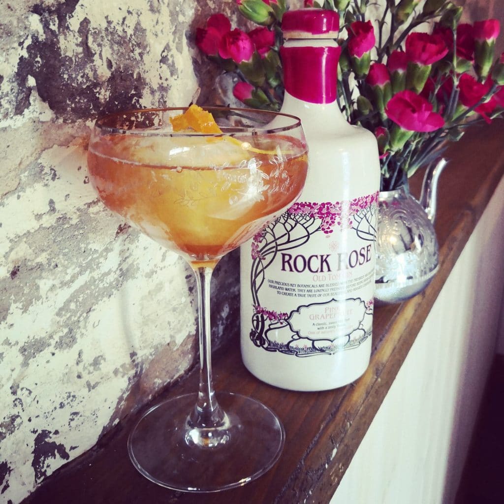 Bottle of Rock Rose Old Tom Gin Pink Grapefruit and Earl of Caithness Collins cocktail served in a coupe glass and garnished with orange peel