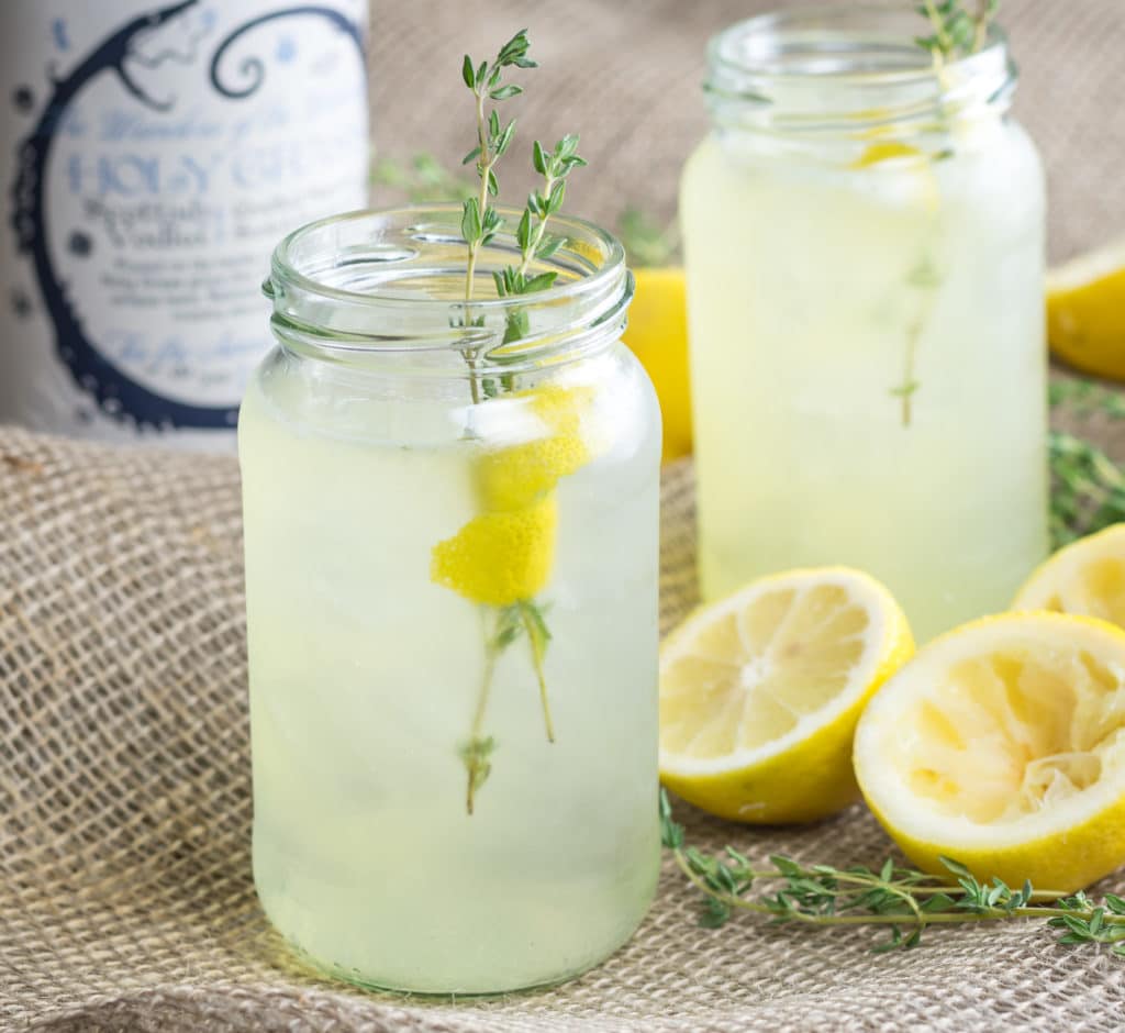 Bottle of Holy Grass Vodka and Me Thyme Cocktail served in two large jars, garnished with lemon peel and thyme sprig