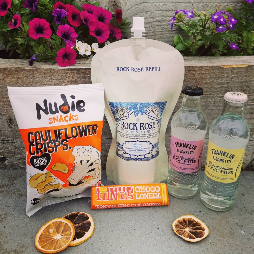 Content of the Refill Rewards Club box for July 2021 including Rock Rose Gin pouch, tonic waters, cauliflower crisps and Tony;s choco lonely bar